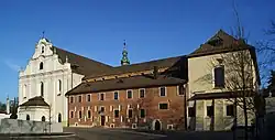 Photographie couleur d'une façade d'église baroque de pierre blanche, à gauche, et de bâtiments en briques à droite