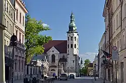 À gauche, les statues des apôtres devant l’église des Saints Apôtres Pierre et Paul et l’église Saint-André. La perspective est fermée par : à droite, l’église Saint-Idzi et en arrière-plan, l’église Saint-Bernardin.