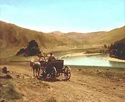  Calèche avec un paysan et deux chevaux longeant une rivière, présumément la Tchouïa, au début du XXe&nbsp;siècle. La scène est représentée sur une carte postale. En arrière-plan se trouve un paysage montagneux.