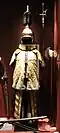 photo d’un mannequin portant un ensemble de tuniques jaune doré et un casque en métal ouvragé
