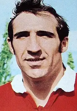 Photographie en couleurs. Portrait d'un homme souriant portant un polo de rugby rouge à col blanc.