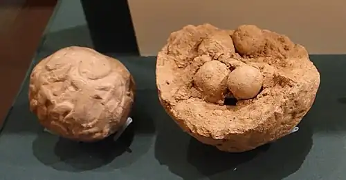 Deux bulles en argile avec des empreintes de sceaux, une complète et l'autre brisée, laissant apparaître des jetons ronds en argile.