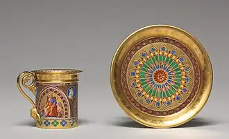 Une tasse et une sous-tasse dorées, à motifs de rois et encadrements géométriques très colorés.