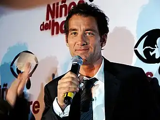 Owen de face tenant un micro devant un logo en espagnol du film.