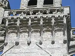 Gros plan en contre-plongée. On voit les arcatures qui soutiennent le rebord de la plate-forme, et la balustrade de celle-ci.