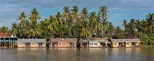 Bungalows colorés flottants de l'hôtel Sala Don Khone, sur la berge du Mékong devant de hauts palmiers, Don Khon en fin d'après-midi, photo prise depuis l'île de Don Det, Laos.