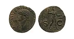 Photographie recto-verso de la copie d'une monnaie. On voit un portrait de profil cerclé d'une inscription d'un côté, et de l'autre un athlète de trois quarts tenant lance et bouclier, avec un "S" et un "C" ainsi que des inscriptions sur le côté.