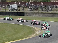 Photographie de monoplaces de F4, dans un virage. Toutes sont sur la même trajectoire.