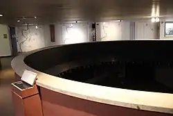 Photographie d'une pièce dont les murs portent des cartes de ville ; au centre, la maquette d'une ville antique.