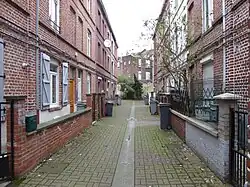 Photographie en couleur représentant deux rangées face à face de petites maisons mitoyennes de trois niveaux avec une poubelle individuelle devant chacune