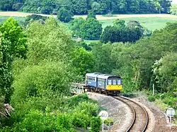Un petit train circule sur une ligne de chemin de fer au milieu de la campagne.