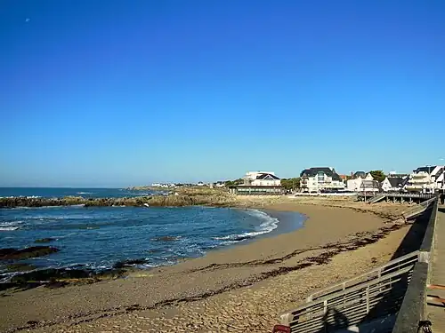 Vue d'une plage de sable, ouverte sur une mer calme sur fond de ciel bleu.