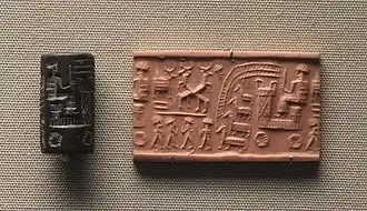 Sceau-cylindre paléo-assyrien avec impression, personnage sur un chariot à quatre roues, tiré par quatre équidés (des ânes ?). Sur la partie gauche, plusieurs personnages et un autel à tête de taureau. British Museum.