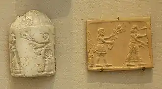 Deux objets sont déposés sur un plan horizontal gris et photographiés de haut. L'un est de pierre blanchâtre et gravé de motifs en creux. L'autre est une plaque d'argile rousse sur laquelle se trouvent des dessins.