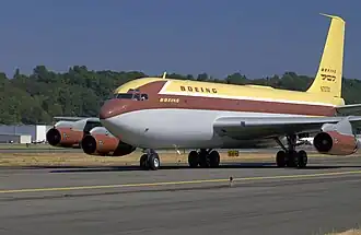Vue de trois-quarts avant d'un avion, roulant sur le tarmac d'un aéroport ; le fuselage est peint de trois couleurs : gris pour sa partie inférieure, jaune sur le dessus avec une ligne de couleur chocolat au niveau des hublots.