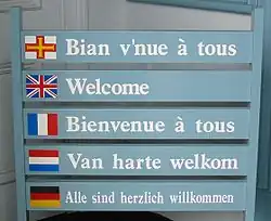 Panneau à Guernesey utilisant le drapeau guernesiais pour représenter la langue de l'île.