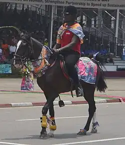 Dans la rue, un cavalier africain portant un casque défile sur un cheval noir.