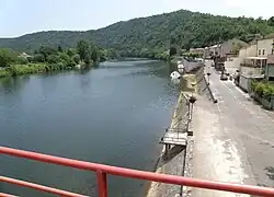La photo couleur montre un mur maçonné qui surplombe la rivière. Une allée bâtie descend en pente douce jusque dans l'eau.