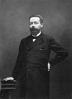 Photographie en noir et blanc d'un homme barbu, de pied.