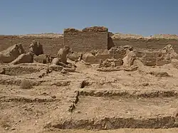Photo en couleur. Dans le désert, des vestiges en pierre sont à l'avant-plan.