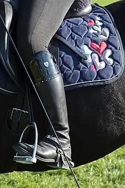 Gros plan sur la botte gauche d'un cavalier reposée sur un étrier tandis que le cavalier est assis sur un cheval noir