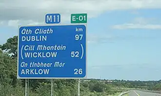 Panneau indicatif de la distance restante à parcourir pour atteindre les villes de Dublin, Wicklow et Arklow surmonté du sigle de l'autoroute irlandaise M11 ainsi que de celui de la route européenne 1