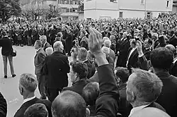 Photographie en noir et blanc d'un groupe d'homme sur une place publique en train de lever le bras droit.