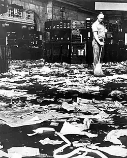 Photo noir et blanc d'un employé balayant une pièce jonchée de papiers abandonnés