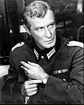Photographie en noir et blanc d'Edward Mulhare en costume d'officier de la Wehrmacht pendant le tournage du film