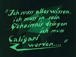 Un écran noir avec des formes vertes délavées en arrière-plan, et des mots verts en langue allemande écrits en caractères d'imprimerie angulaires au premier plan.
