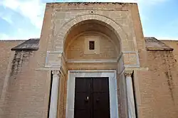 Photographie d'un porche de la façade orientale. Celui-ci est ouvert par un arc en plein cintre outrepassé.