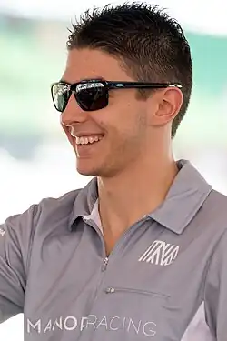Photographie d'un homme brun, souriant, vu de trois-quarts, en gros plan, avec des lunettes de soleil.