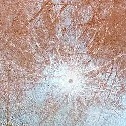 Zoom sur le cratère. Un petit point brun est visible, entouré de lignes blanches partant dans toutes les directions depuis celui-ci.