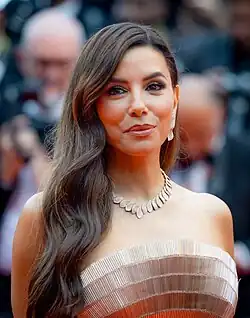 Photographie en couleur du visage l'actrice, cheveux longs noirs et souriante.