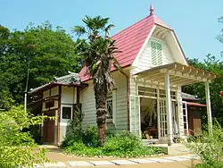 Maison blanche à toit rouge entourée de végétation.