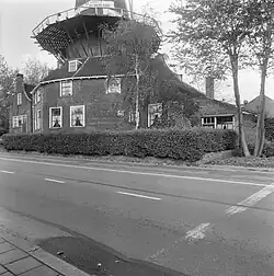 Photographie en noir et blanc d'une maison et d'une remise couronnés d'une galerie et longées par une route.