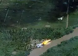 Photo couleur d'un avion en vol, avec une boule de feu au sol.