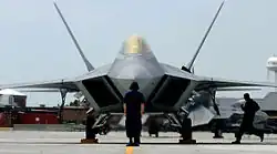 Photo d'un F-22 vu de face. Un mécanicien se tient debout devant lui, donnant un sens de l'échelle, un autre court sur le côté de l'avion.