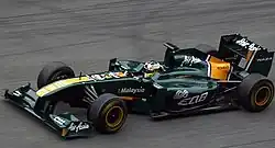 Photographie d'une monoplace de Formule 1 vert foncé, vue dans son ensemble, de haut, de trois-quarts, sur une piste sèche.