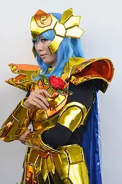 Homme aux cheveux bleus portant une armure dorée et un rose rouge entre les doigts.