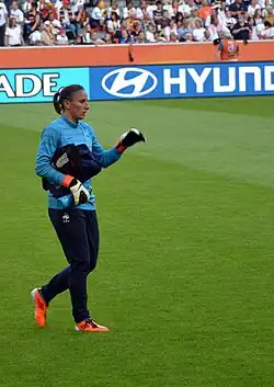 Photographie d'une gardienne de but, vue de profil, habillée en bleu, en plan d'ensemble.