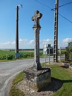 Une croix en pierre, sans ornement remarquable, au bord d'une route.