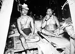 Photo en noir et blanc figurant des hommes assis en tailleur dans une maison en bois.