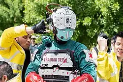 Photo en buste d'une personne déguisée avec une tenue verte et blanche, et un casque blanc et vert avec de multiples capteurs.