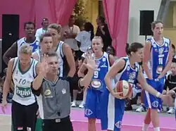 L'arbitre, tourné signale le numéro de la joueuse fautive à la table de marque. Dans son dos, des joueuses discutent la décision.