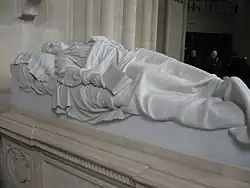 gisant en marbre blanc d'un jeune homme tenant un livre dans la main droite.