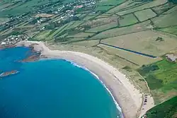 Une grande plage arrondie sépare la mer d'une prairie humide, drainée par deux canaux.