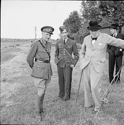 Sur fond de paysage de campagne, le général Montgomery (âgé d'une cinquantaine d'années, en uniforme) et Winston Churchill (une soixantaine d'années, en civil) entourent Pierre II (âgé d'environ 18&nbsp;ans, en uniforme).