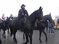 Cavaliers sur des chevaux noirs et portant des manteaux de pluie amples.