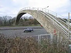 Photo d'une arche en béton avec des marches et des barrières de sécurité qui passe au-dessus d'une route à plusieurs voies sur laquelle circule une voiture